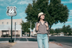 young lady traveler standing in front of the famous sign route 66 post office. asian woman tourist with straw hat visits the town in sunshine day. elegant girl enjoy the beauty of the sky.